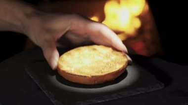 Prepare a burger against the background of fire close-up. Stone tray. Spot lighting. Bun, cheese, lettuce.