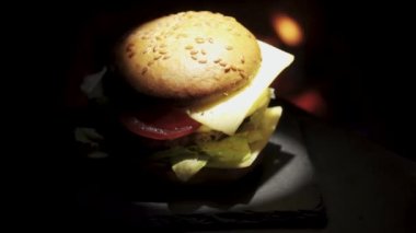 The burger rotates and lights smoothly against the background of the fire. On a stone tray. Spot lighting.