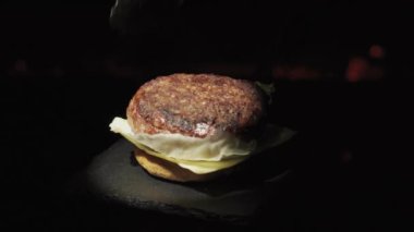 Prepare a burger against the background of fire close-up. Stone tray. Spot lighting. Catlet and becon