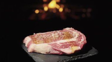 A rotating piece of steak on the background of fire. Sprinkle with olive oil