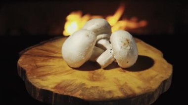 Three mushrooms Champignon on a wooden tray. Rotation against the background of fire, olive oil