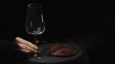 Table setting against the background of fire. A glass of red wine and a steak with rosemary. Spotlight.