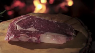 Close-up steak spinning on a wooden tray against the background of fire. I put the rosemary