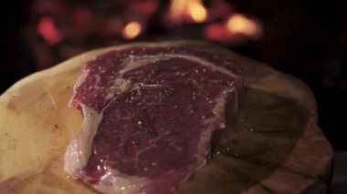 Close-up steak spinning on a wooden tray against the background of fire. Sprinkle with pepper