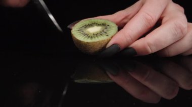 The girl pulls out the pulp of a kiwi, the camera zooms in close-up, on a black background.