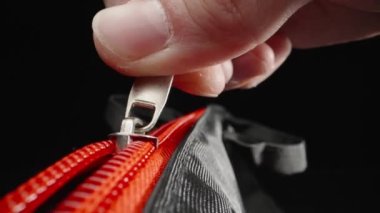 Extreme close-up of fingers fastening a red zipper. Laowa Probe, black background