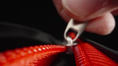 Extreme close-up of fingers fastening a red zipper. Laowa Probe, black background