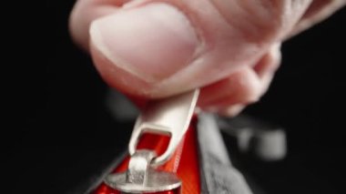 Extreme close-up of fingers fastening a red zipper. Laowa Probe, black background