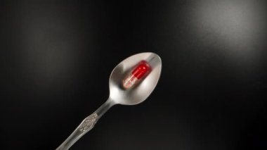 Red and white pill, capsule on a spoon, black background, top view. Dolly slider extreme close-up. Laowa Probe