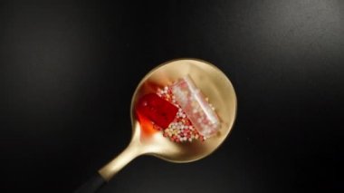 Red and white opened pill, capsule on a spoon, black background, top view. Dolly slider extreme close-up. Laowa Probe