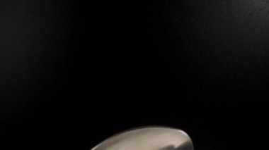 White round pills fall on a spoon, black background, top view. Dolly slider extreme close-up. Laowa Probe