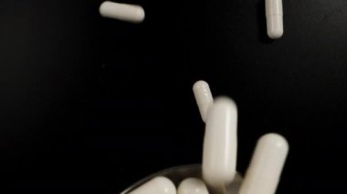 White capsule pills fall on a spoon, black background, top view. Dolly slider extreme close-up. Laowa Probe