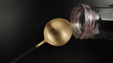 I pour red syrup from a bottle on a golden spoon, black background, top view. Dolly slider extreme close-up. Laowa Probe