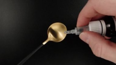 I drip medicine from a pipette on a golden spoon, black background, top view. Dolly slider extreme close-up. Laowa Probe