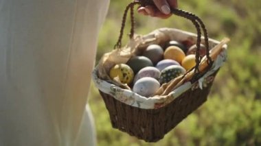 A woman holds a knitted basket with painted Easter eggs. in the forest on the background of green grass, a view in a circle.