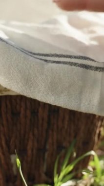 A wicker basket stands by a tree in a sunny forest. I pick up the towel, and there are Easter eggs in the basket, decorated. close-up. Vertical video Social Media