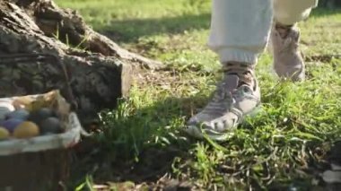 A girl in the Forest approaches a basket with Easter Eggs, covers them with a towel and takes them away.