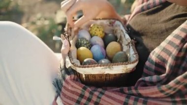 Close-up of a girl who is sitting and holding a basket with Easter decorated eggs. Sunny.