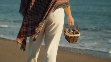 A woman with a basket of Easter Eggs walks on the sand, stops and looks into the sea.