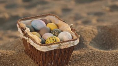 Sunset on the beach. On the sand there is a wicker basket in which Painted Easter eggs, a panorama close-up.