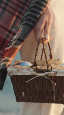 A girl admires the sunset on the sea beach and holds a basket with Painted Easter Eggs. Slow motion. Vertical video Social Media