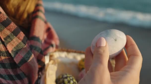 少女はイースターの卵のバスケットを保持し 彼女の手で1つを調べる波の横に立っている — ストック動画