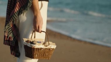 The girl stands covered with a blanket at sunset by the sea. Holding a basket of Easter Eggs