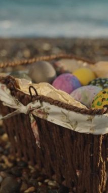 A wicker basket with Easter eggs on the rocks by the sea. Sunset, slow motion. Vertical video Social Media