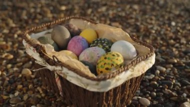 A wicker basket with Easter eggs on a pebble by the sea. Tilt, slow motion. Close-up