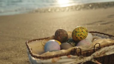 Wicker basket with Easter eggs on the beach by the sea. Panorama, slow motion. Close-up, sun rays and waves.