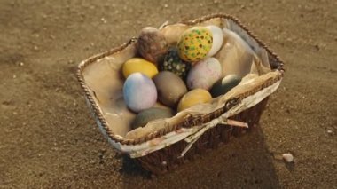 Basket with Decorated Easter eggs on the sand, close-up, Tilt.