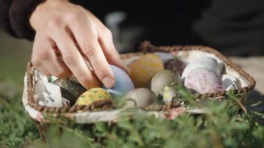Knitted basket with Easter eggs, in the grass. I take and examine the eggs one by one. Close-up.