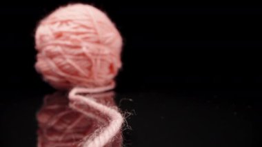 A ball of pink woolen threads, on black glass.. Dolly slider extreme close-up. Laowa Probe