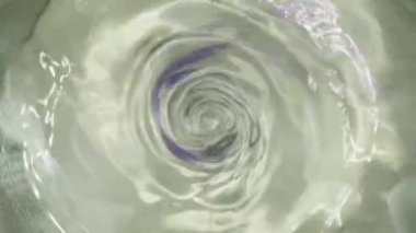 Whirlpool or funnel in water. macro shooting, slow motion. Purple sparkles fly into the water