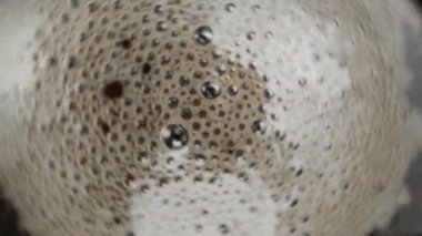 Coffee foam and bubbles spin in the cup as the camera zooms out. Macro shooting, slow motion