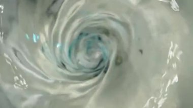 Whirlpool or funnel in water. macro shooting. Water turns blue, slow motion.