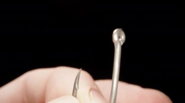 I am threading a braided fishing line into the ring of a fishing hook, close-up.