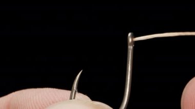 I am threading a braided fishing line into the ring of a fishing hook, close-up.