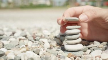 Close-up, a woman makes a cairn. Handmade stone tower on the seashore. A stack of balanced pebbles on the beach.