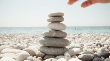 Yakın plan, bir kadın cairn yapıyor. Deniz kıyısında el yapımı taş kule. Sahilde bir yığın dengeli çakıl taşı. Denizin arka planına karşı