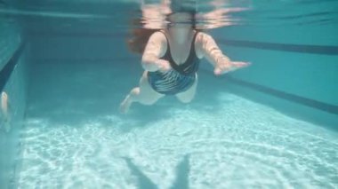 Blue swimming pool, underwater shooting, sunny day. A plump young woman swims in a closed swimsuit