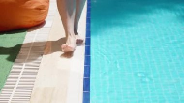 Blue pool, sunny day. young woman along the pool and wets her foot in the water. Slow motion