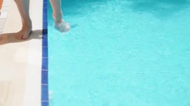 Blue pool, sunny day. young woman along the pool and wets her foot in the water. slow motion. Slow motion