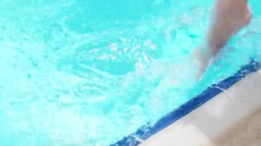 Blue pool, sunny day. young woman splashing her feet in the wate. Slow motion, close up.