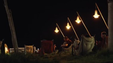 Night city, people relax in a cafe on the seashore, under the lights on the chairs.