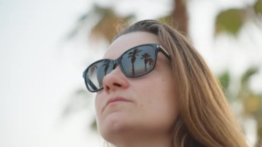 reflection of a palm tree in the young woman 's sunglasses, close-up