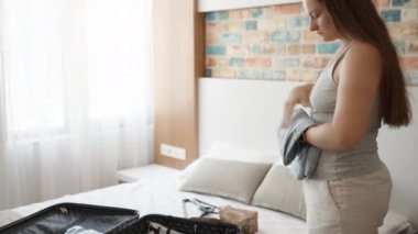 The young woman packs her things on the bed in a suitcase. Sunny day
