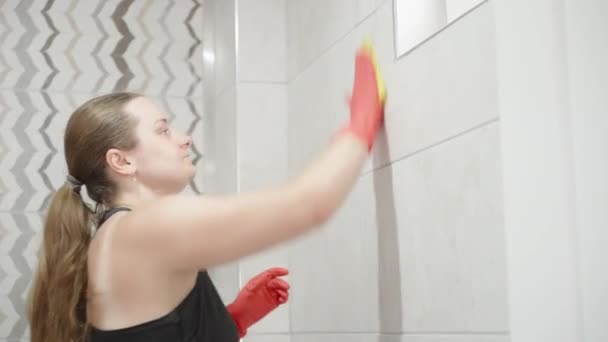 一个戴着红色手套 留着长发的年轻女人 浴室里洗瓷砖 — 图库视频影像