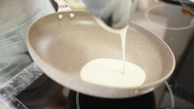 The young woman pours pancake dough into a frying pan. Close-up. Slow mo