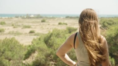 Long hair blows in the wind. young woman is looking at the sea in the distance. Slow mo